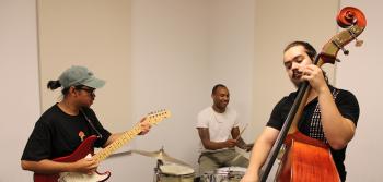 Three students play guitar, upright bass, and drums together.