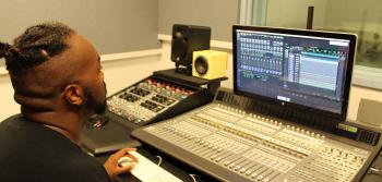 A student works in front of a mixing console and computer running Pro Tools software.