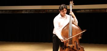 A student plays an upright bass with a bow on the Alpert Recital Hall stage.
